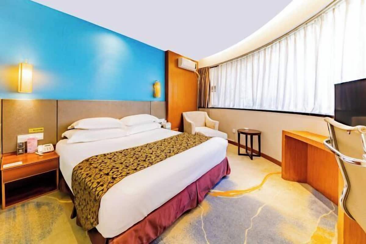 Une chambre d’hôtel avec un grand lit, un bureau, une chaise, une télévision et une fenêtre avec des rideaux.