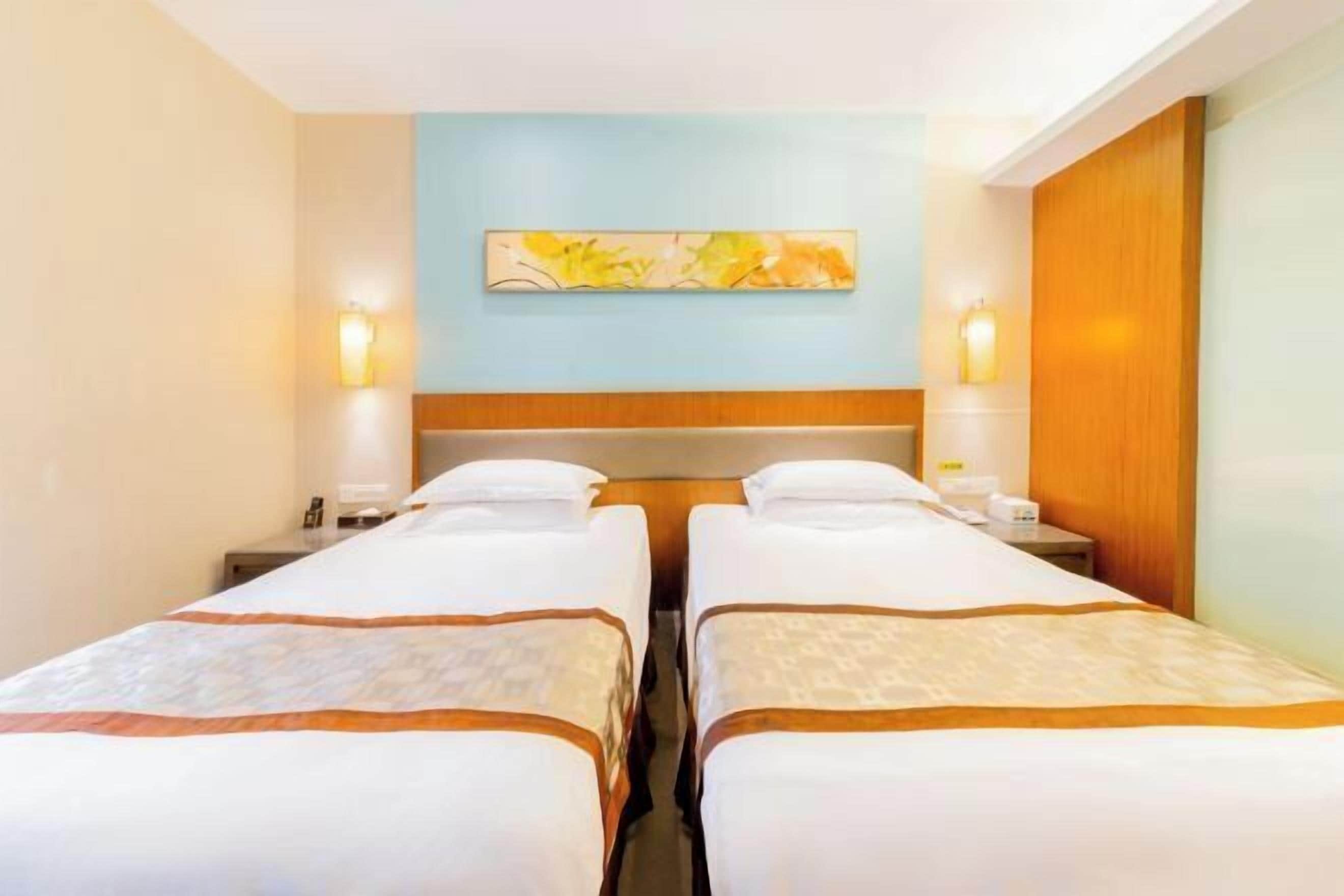 A hotel room with two beds, a light blue accent wall, and a painting above the beds.