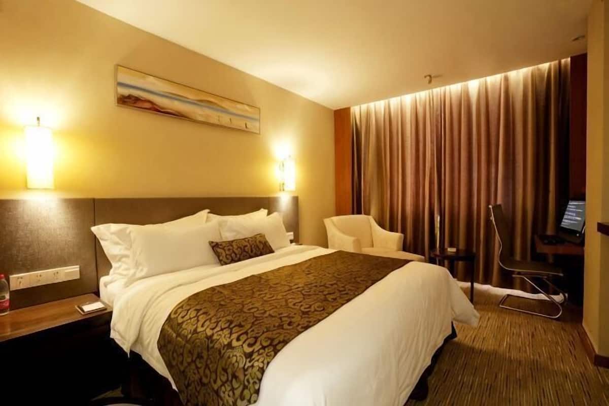Une chambre d’hôtel avec un grand lit, un bureau, une chaise, une lampe de bureau et un téléviseur.