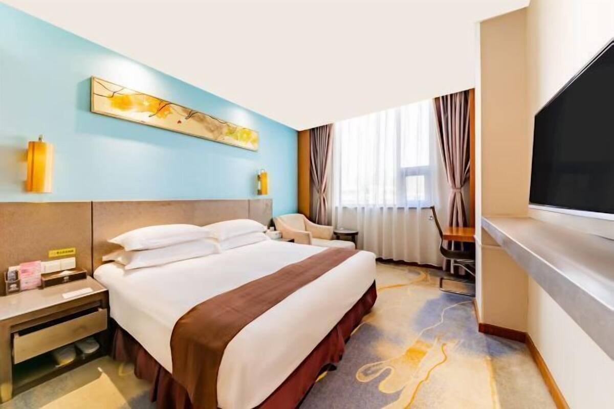 Une chambre d’hôtel équipée d’un lit, d’un bureau, d’une chaise, d’une télévision et d’une fenêtre avec des rideaux.
