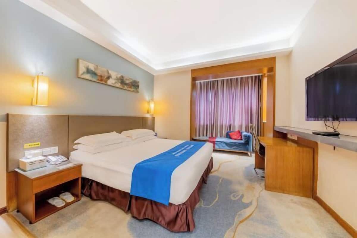 Une chambre d’hôtel avec un grand lit, une table de chevet, une lampe et un téléviseur.