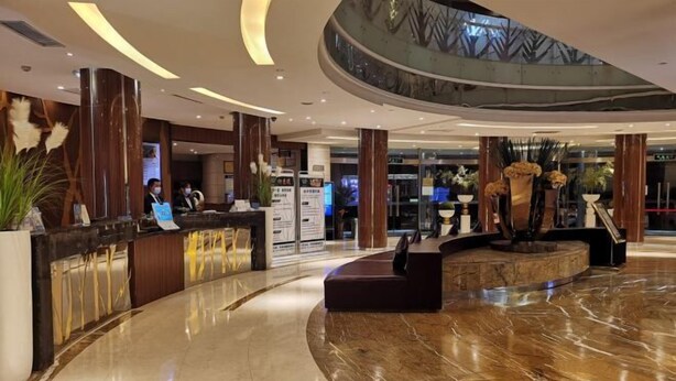 Een moderne hotellobby met een marmeren vloer, een receptiebalie en decoratieve planten.