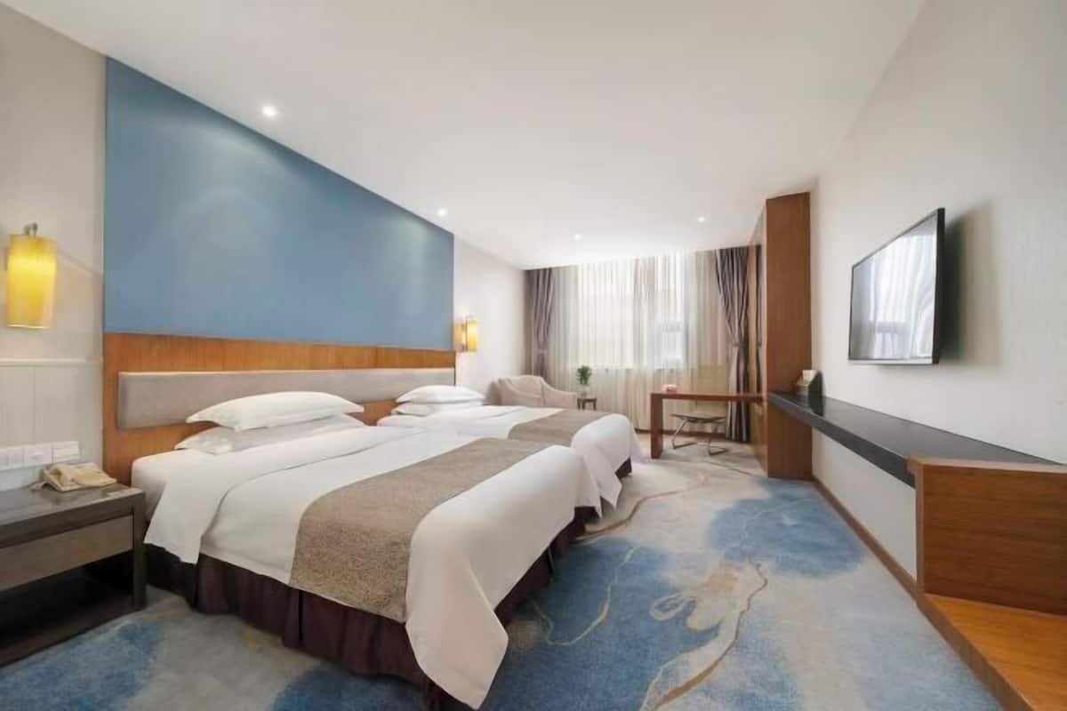 Une chambre d’hôtel avec deux lits, un bureau, une chaise, une télévision et une grande fenêtre avec des rideaux.
