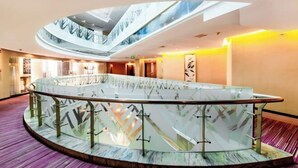 Een moderne hotellobby met een glazen balustrade in het midden, een hoog plafond met dakramen en een paars vloerkleed.