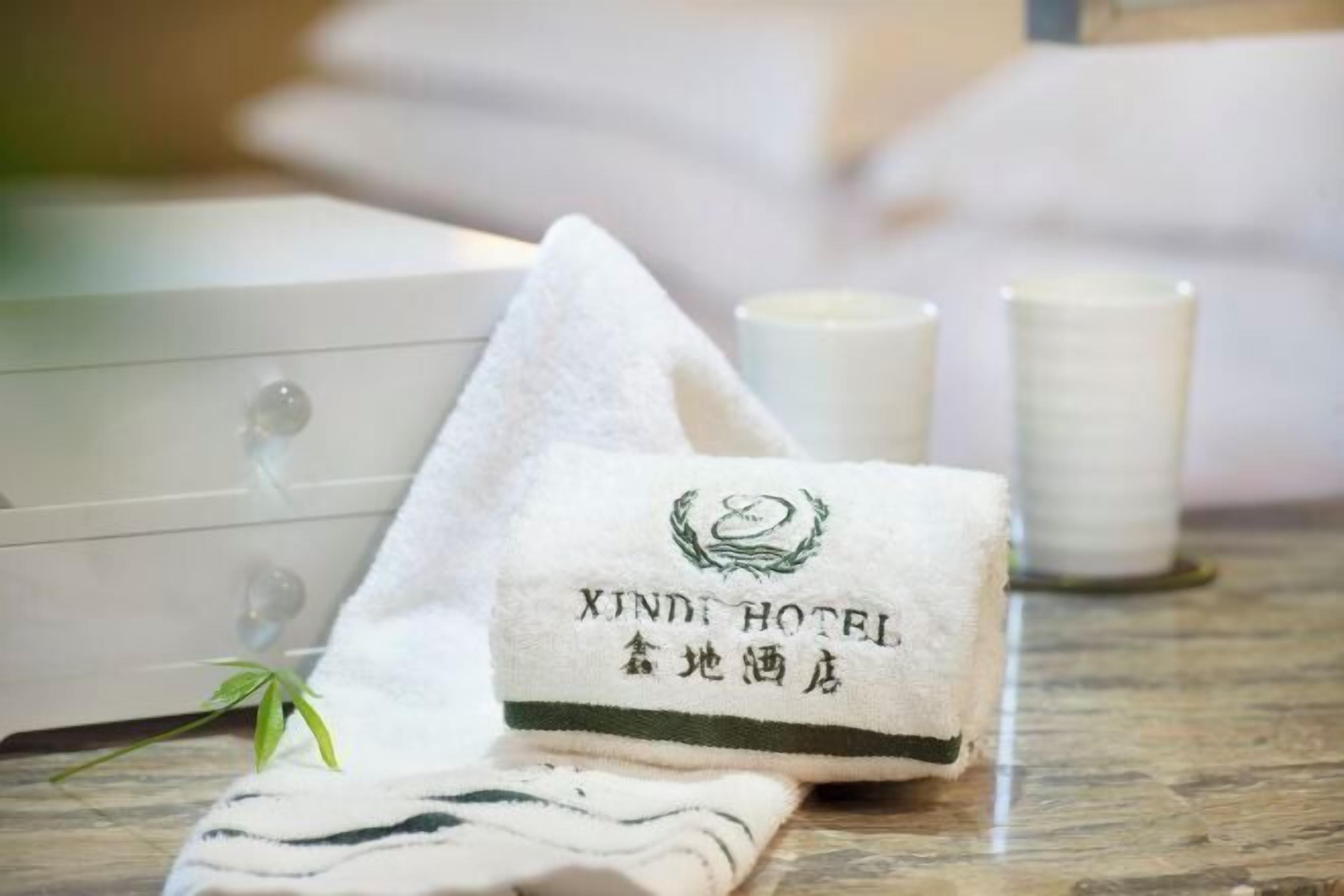 A neatly folded towel with "XINDI HOTEL" branding, a small green plant, and two candles on a marble surface.