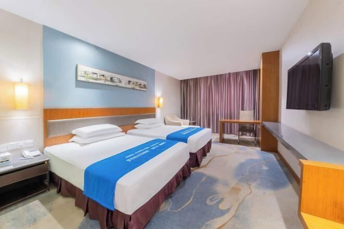 Une chambre d’hôtel avec deux lits, un bureau, une chaise, une télévision et une œuvre d’art accrochée au mur.