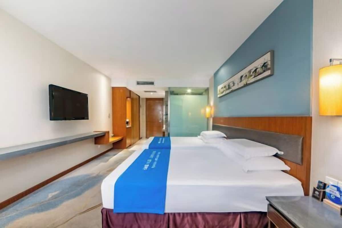 Une chambre d’hôtel avec un lit, un téléviseur à écran plat fixé au mur, une table de chevet et un couvre-lit bleu.