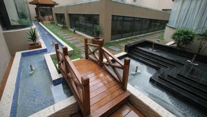A modern hotel courtyard with a wooden bridge, a small pool, and a Zen garden.
