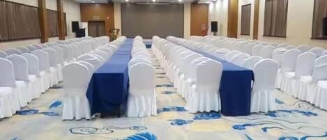 A conference room with rows of white chairs, a blue table, and a patterned carpet.