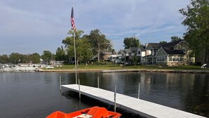 Un lac avec un quai, un petit bateau et des maisons en arrière-plan.