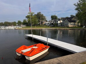A lake with a dock, a small boat, and houses in the background.