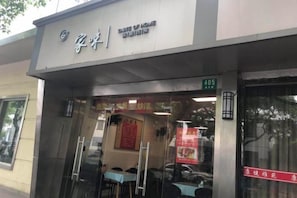 A restaurant with a glass entrance and outdoor seating visible through the windows. - Changee Hotel (Shanghai Baoshan Wanda Gongkang Road Subway Station) (Shanghai)