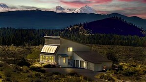 A modern house with a sloped roof, large windows, and a garage, surrounded by forest and mountains. - Sundance Ranch Retreat | Hot Tub • Cascade Views (Deschutes County)