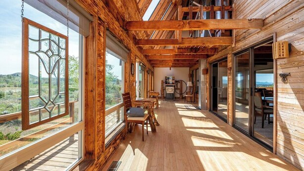 A wooden cabin with a balcony, large windows, and a dining area. - Sundance Ranch Retreat | Hot Tub • Cascade Views (Deschutes County)