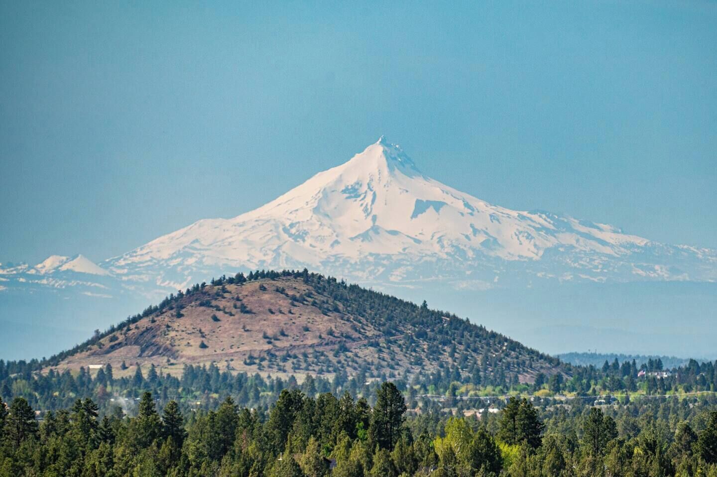 A mountain with a snow-covered peak and a forested valley below.