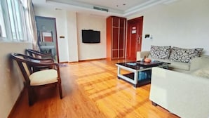 A living room with a wooden floor, a sofa, a chair, a coffee table, and a television.