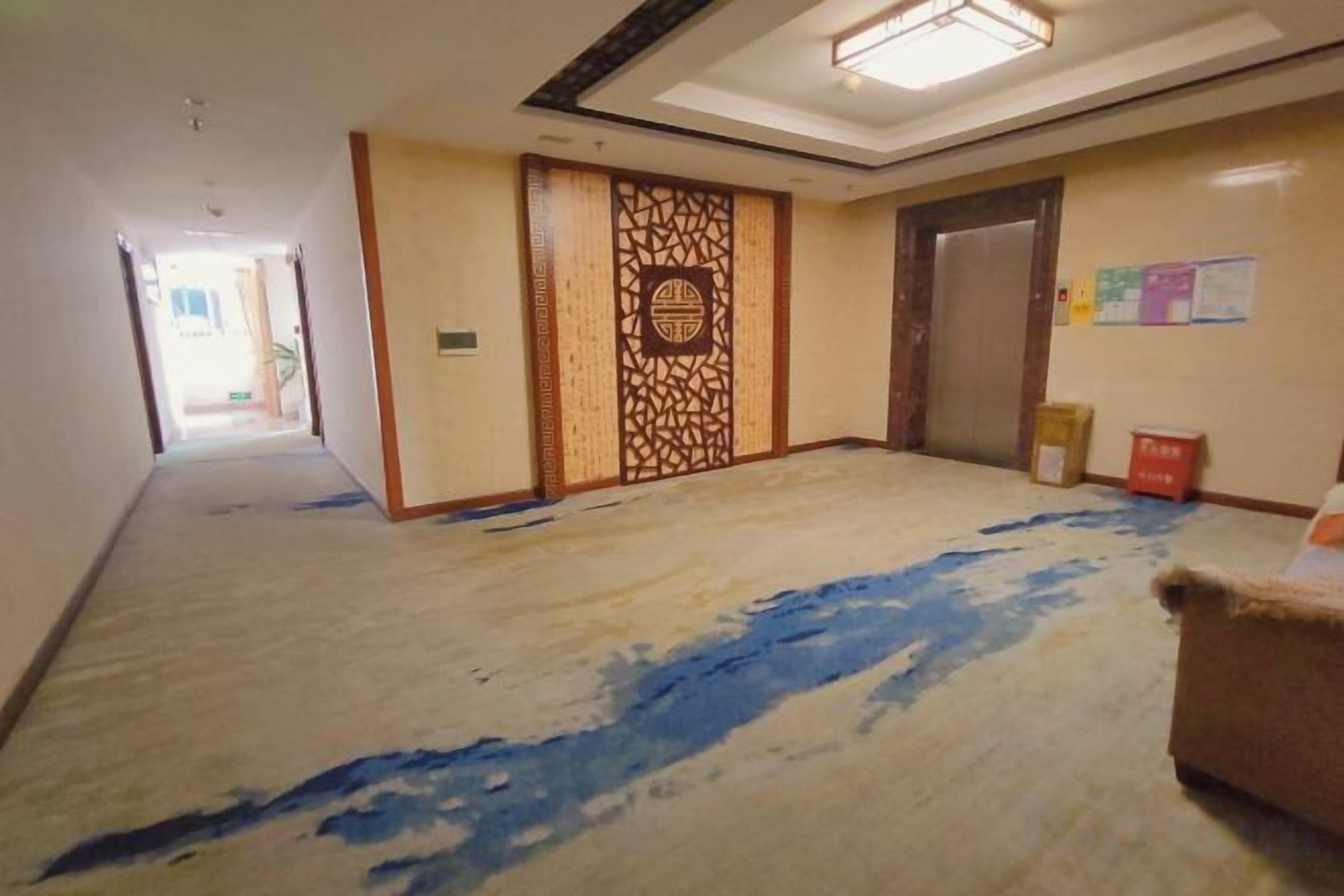 Corredor de hotel com piso revestido de carpete, painel decorativo na parede e uma porta.