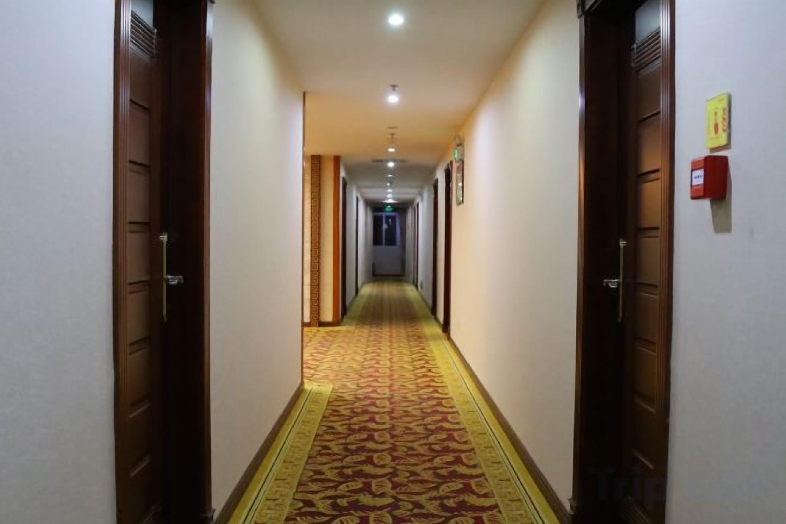A hotel hallway with carpeted floors, wooden doors, and a fire alarm on the wall.