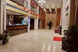 Un hall de hotel con mostrador de recepción, plantas en macetas y alfombra roja.