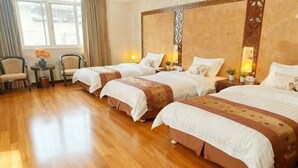 A hotel room with two beds, a wooden floor, a small table with chairs, and a window with curtains.