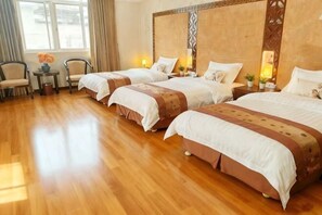Ein Hotelzimmer mit zwei Betten, Holzboden, einem kleinen Tisch mit Stühlen und einem Fenster mit Vorhängen.