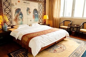 Une chambre d’hôtel avec un grand lit, deux tables de chevet avec des lampes, une chaise, une petite table et un mur décoratif.