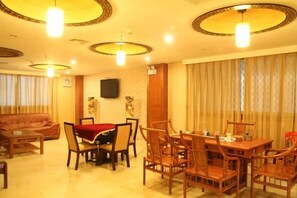 A dining area with a table set for four, surrounded by wooden chairs, a sofa, and a television on the wall. - Jinmei Hotel (Jiaoling)