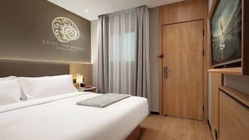 A hotel room with a bed, a television, a door, and a wall with a logo.