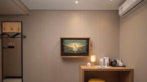 Ein Hotelzimmer mit einem Holztisch, einem kleinen Hocker, einem gerahmten Kunstwerk an der Wand und einem Spiegel mit Holzrahmen.