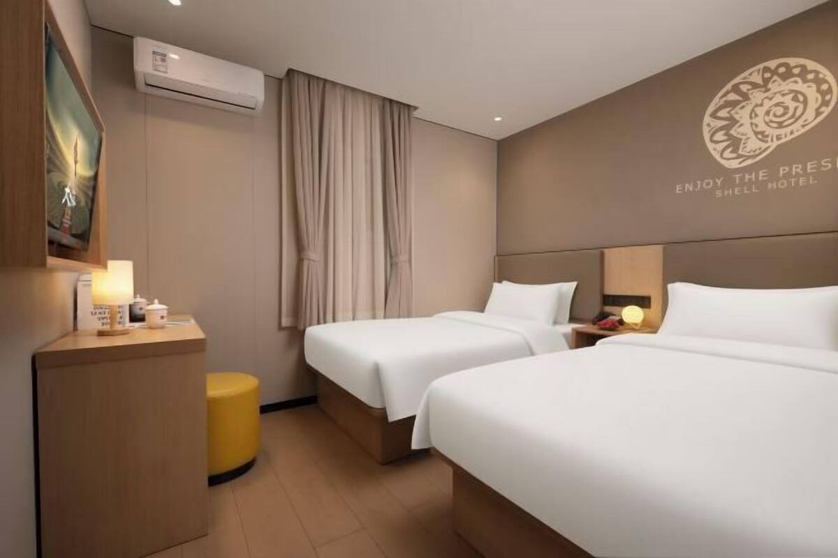 Ein Hotelzimmer mit zwei Betten, einem Schreibtisch, einem Sessel, einer Klimaanlage und einer Wand mit dem Namen des Hotels.