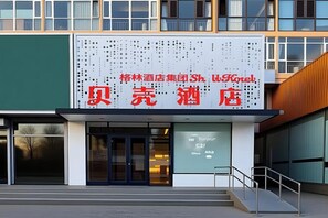 A hotel entrance with a signboard displaying the name in red characters, a glass door, and a staircase leading to the entrance. - Shell Hotel (Shunyi Ideal Automobile Base, Beijing) (Beijing)
