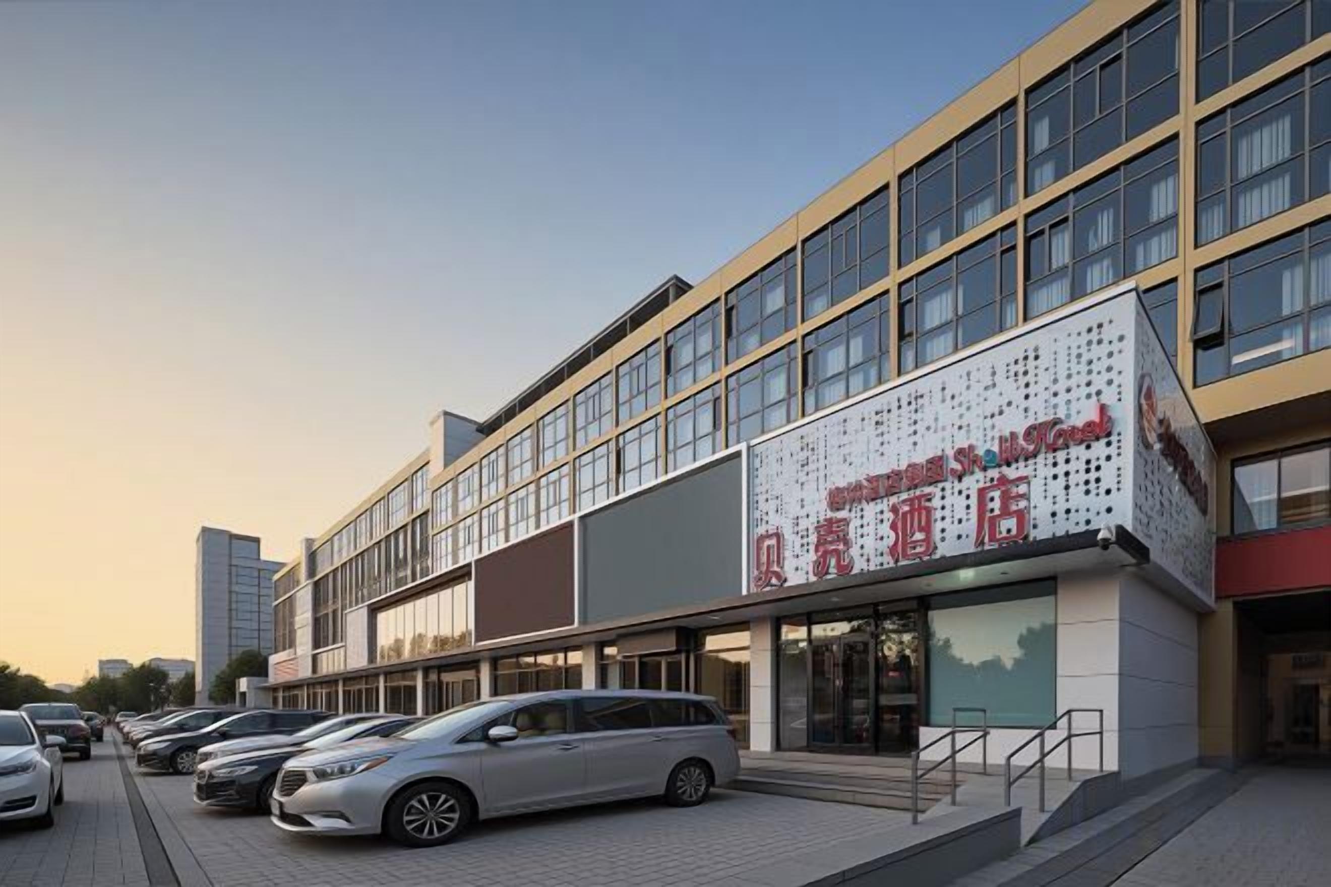 A multi-story building with a large signboard, a parking area with several cars, and a clear sky.