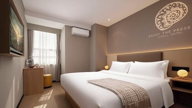 Ein Hotelzimmer mit einem großen Bett, einem Nachttisch mit Lampe, einer Wandklimaanlage und einem gerahmten Bild an der Wand.
