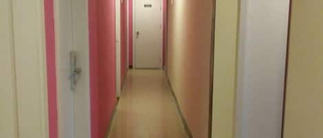 A narrow hallway with doors on both sides, leading to a room at the end.