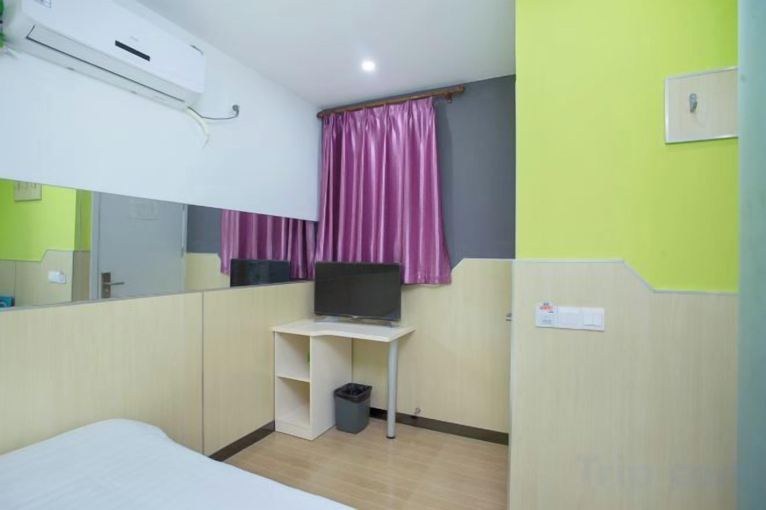 A hotel room with a bed, a desk with a computer, a mirror, and a window with curtains.