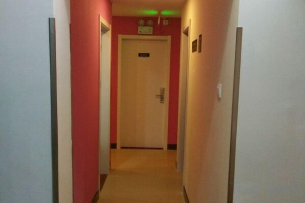 A narrow hallway with a door at the end, a light switch, and a wall-mounted light fixture.