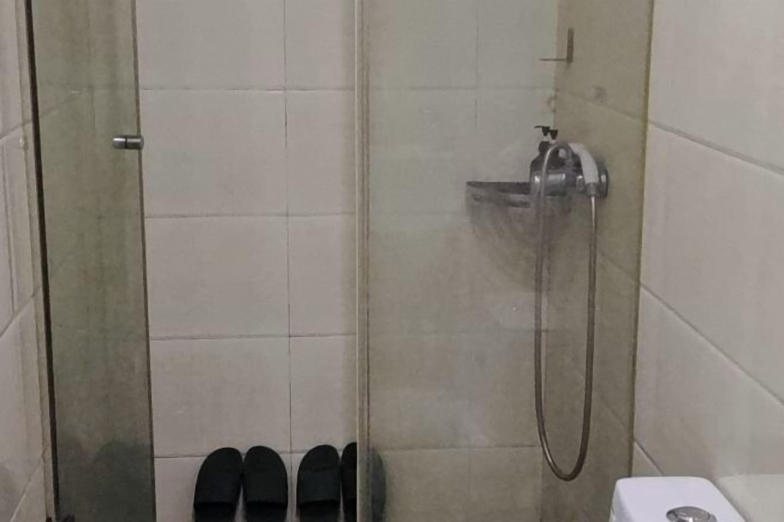 Un espacio de ducha con puerta de cristal, un cabezal de ducha manual y un par de zapatillas negras en el suelo.