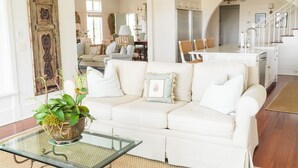 Ein geräumiges Wohnzimmer mit einem weißen Sofa, einem Glastisch und einer Zimmerpflanze.