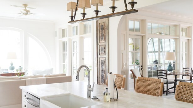 Eine helle Küche mit weißer Arbeitsplatte, integriertem Geschirrspüler und modernem Wasserhahn. Es gibt einen Essbereich mit Korbstühlen und einem Tisch.