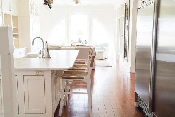 A modern kitchen with white cabinetry, a stainless steel refrigerator, and a dining area with a bench.