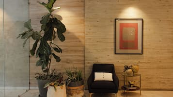 A modern room with a wooden wall, a framed abstract painting, a black armchair with a white pillow, and several potted plants.