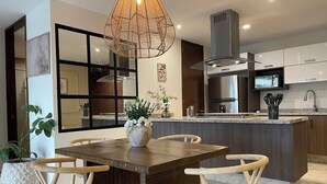 Une cuisine moderne dotée d’un îlot central, de chaises en bois foncé, d’un grand luminaire suspendu et d’une hotte de cuisine en acier inoxydable.