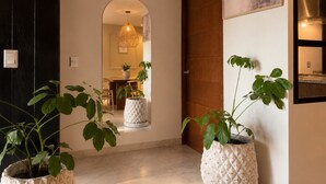 Un couloir avec une porte en bois, un miroir, un luminaire suspendu et des plantes en pot.