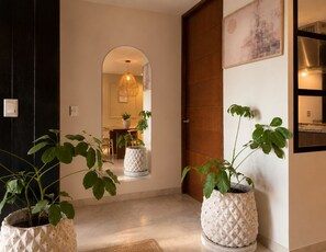 A hallway with a wooden door, a mirror, a hanging light fixture, and potted plants. - Financial Upper Suite / Daily Clean (guadalajara)