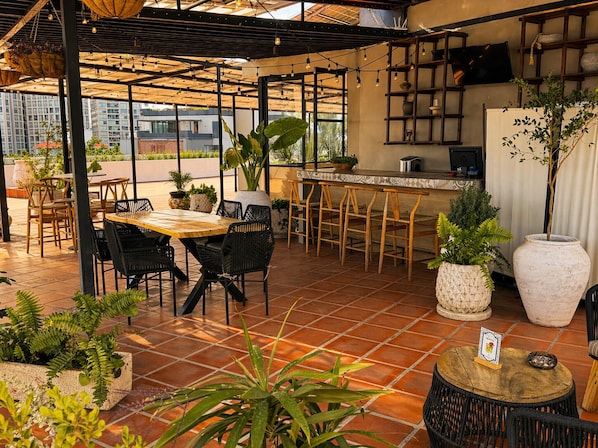 Un espace extérieur aménagé en terrasse, avec une table et des chaises en bois, un comptoir de bar et diverses plantes en pot.