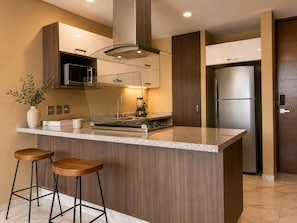 A modern kitchen with a central island, bar stools, a microwave, a stove, and a refrigerator.