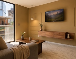 A modern living room with a sofa, coffee table, and a mounted TV displaying a mountain landscape.