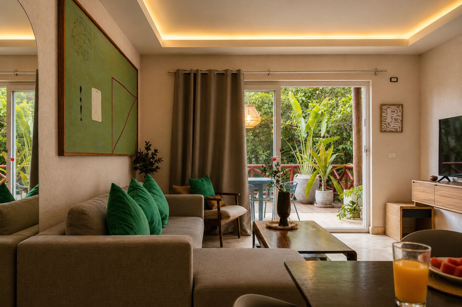 Una sala de estar con sofá, mesa de centro y televisor. Hay una puerta corrediza de vidrio que da a un área exterior con plantas.