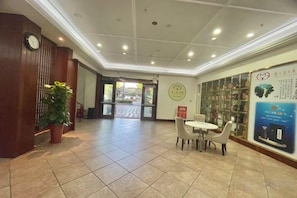 A hotel lobby with a reception desk, a potted plant, a seating area, and a wall with informational posters.