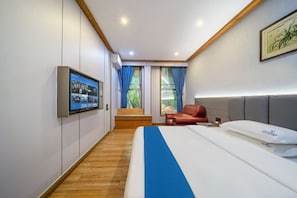 Une chambre d’hôtel avec un lit, un téléviseur fixé au mur, une fenêtre avec des rideaux et un tableau encadré accroché au mur.